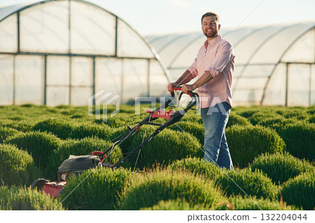 With lawn mower. Adult farmer is outdoors With lawn mower. Adult farmer is outdoors 132204044