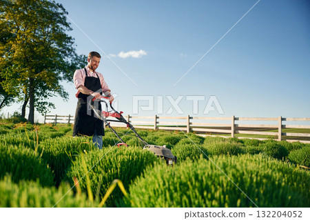 Cleaning the field by using lawn mower. Adult farmer is outdoors Cleaning the field by using lawn mower. Adult farmer is outdoors 132204052