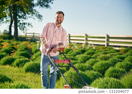 Red colored lawn mower. Adult farmer is outdoors 132204077