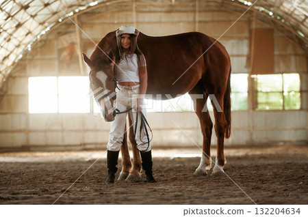 In the cowboy hat. Beautiful young woman is with horse indoors In the cowboy hat. Beautiful young woman is with horse indoors 132204634