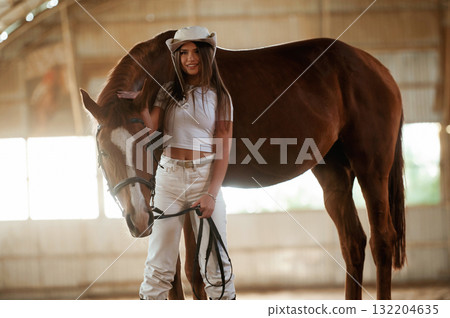 In the cowboy hat. Beautiful young woman is with horse indoors 132204635