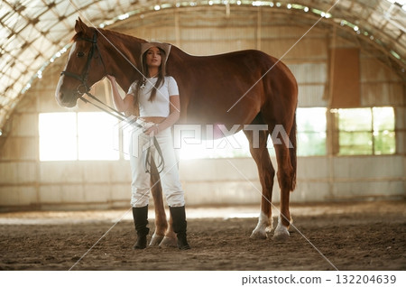 Standing and posing. Beautiful young woman is with horse indoors 132204639