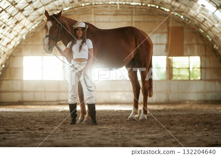 Standing and posing. Beautiful young woman is with horse indoors 132204640