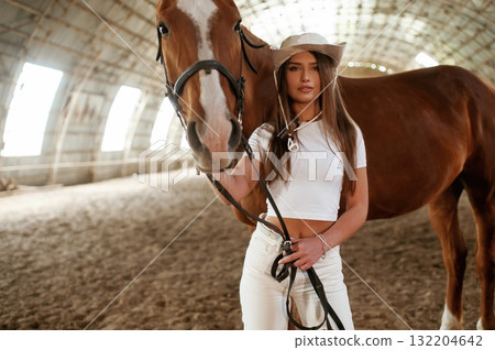 Looking forward. Beautiful young woman is with horse indoors Looking forward. Beautiful young woman is with horse indoors 132204642