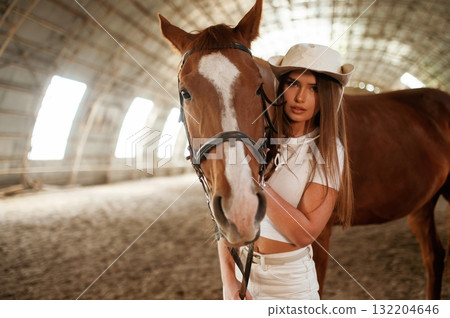 Looking forward. Beautiful young woman is with horse indoors Looking forward. Beautiful young woman is with horse indoors 132204646