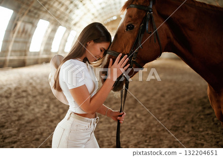 Embracing the animal. Beautiful young woman is with horse indoors Embracing the animal. Beautiful young woman is with horse indoors 132204651