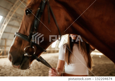 Behind an animal. Beautiful young woman is with horse indoors Behind an animal. Beautiful young woman is with horse indoors 132204674