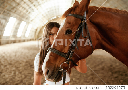 Behind animal head. Beautiful young woman is with horse indoors 132204675