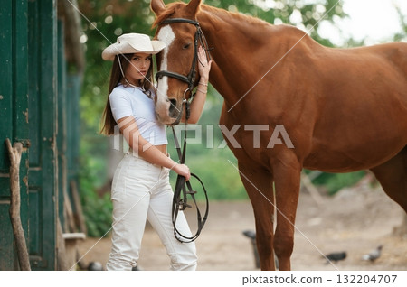 Woman is in hat, side view. With a horse outdoors Woman is in hat, side view. With a horse outdoors 132204707