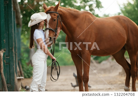 Woman is in hat, side view. With a horse outdoors Woman is in hat, side view. With a horse outdoors 132204708