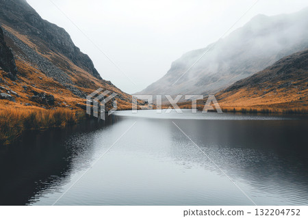 serene lake surrounded by misty mountains, soft grey tones, and crisp reflections create tranquil atmosphere 132204752