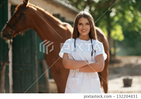 With stethoscope. Female vet is with horse outdoors at the farm at daytime With stethoscope. Female vet is with horse outdoors at the farm at daytime 132204831