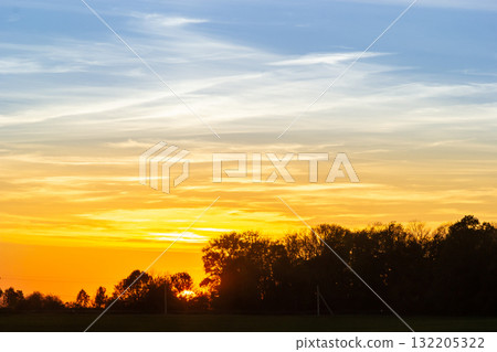 Stunning sunset over a tranquil landscape with vibrant colors and silhouettes of trees in the distance Stunning sunset over a tranquil landscape with vibrant colors and silhouettes of trees in the distance 132205322