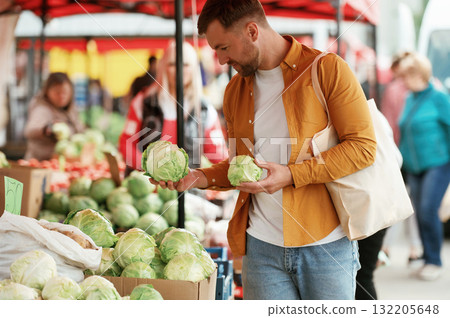 Choosing cabbage. Handsome man is on the street market or bazaar Choosing cabbage. Handsome man is on the street market or bazaar 132205648