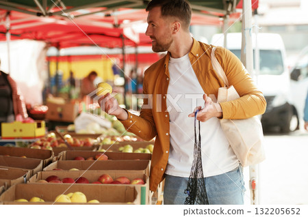Taking an apple. Handsome man is on the street market or bazaar 132205652