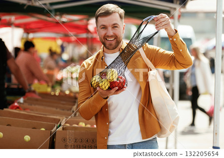 Pepper and apples, smiling. Handsome man is on the street market or bazaar 132205654