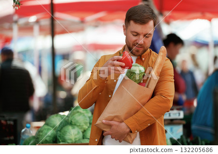 Baguette, pepper and cabbage in bag. Handsome man is on the street market or bazaar 132205686