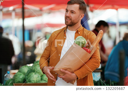 Baguette, pepper and cabbage in bag. Handsome man is on the street market or bazaar 132205687