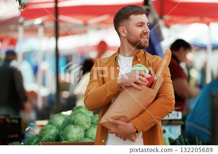 Baguette, pepper and cabbage in bag. Handsome man is on the street market or bazaar Baguette, pepper and cabbage in bag. Handsome man is on the street market or bazaar 132205689
