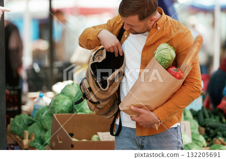Opening the backpack. With products in paper bag. Handsome man is on the street market or bazaar Opening the backpack. With products in paper bag. Handsome man is on the street market or bazaar 132205691