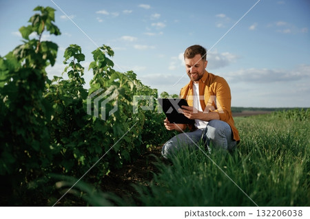 Documents in hand. Handsome man is on the agricultural field at daytime Documents in hand. Handsome man is on the agricultural field at daytime 132206038