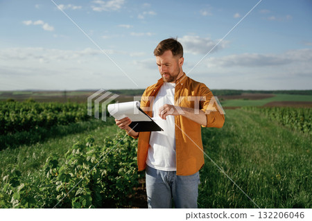 Documents in hand. Handsome man is on the agricultural field at daytime 132206046