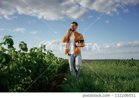 Talking by phone, holding notepad. Handsome man is on the agricultural field at daytime Talking by phone, holding notepad. Handsome man is on the agricultural field at daytime 132206051