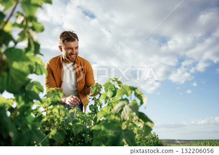 Positive emotion, looking at bush. Handsome man is on the agricultural field at daytime Positive emotion, looking at bush. Handsome man is on the agricultural field at daytime 132206056