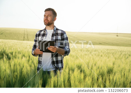 Digital tablet in hands. Handsome man is on the agricultural field at daytime Digital tablet in hands. Handsome man is on the agricultural field at daytime 132206073