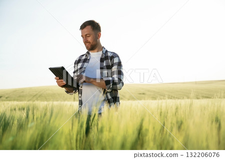 Black digital tablet in hands. Handsome man is on the agricultural field at daytime 132206076