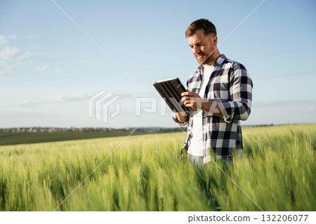 Black digital tablet in hands. Handsome man is on the agricultural field at daytime 132206077