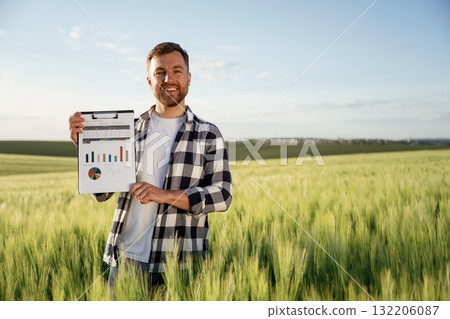Successful businessman with graphs on notepad is standing on the agricultural field at daytime Successful businessman with graphs on notepad is standing on the agricultural field at daytime 132206087
