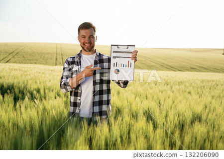 Successful businessman with graphs on notepad is standing on the agricultural field at daytime Successful businessman with graphs on notepad is standing on the agricultural field at daytime 132206090