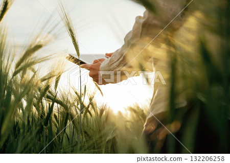 Particle view, holding digital tablet. Woman in white is on the agricultural wheat field 132206258