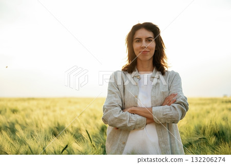Standing with arms crossed. Woman in white is on the agricultural wheat field Standing with arms crossed. Woman in white is on the agricultural wheat field 132206274