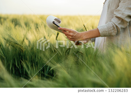 Notepad with documents in hands. Woman in white is on the agricultural wheat field Notepad with documents in hands. Woman in white is on the agricultural wheat field 132206283