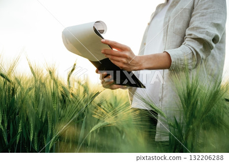 Side view, holding notepad with documents. Woman in white is on the agricultural wheat field Side view, holding notepad with documents. Woman in white is on the agricultural wheat field 132206288
