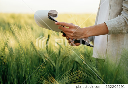 Side view, holding notepad with documents. Woman in white is on the agricultural wheat field 132206291