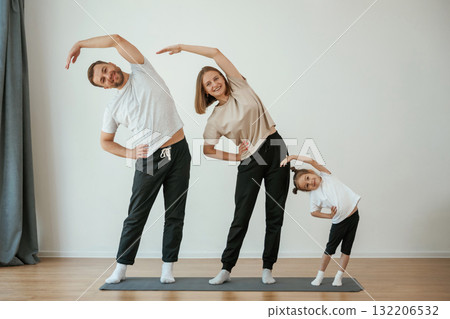 Warm up exercises. Family of mother, father and daughter are doing yoga at home 132206532