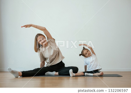 To the side, stretching. Young woman with little girl are doing yoga at home To the side, stretching. Young woman with little girl are doing yoga at home 132206597
