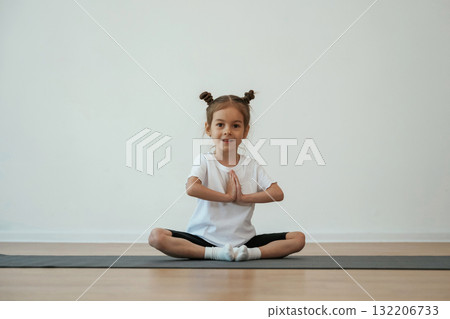Cute little girl is sitting on the yoga mat and doing exercises Cute little girl is sitting on the yoga mat and doing exercises 132206733