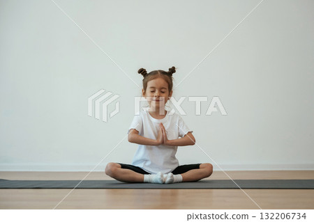 Cute little girl is sitting on the yoga mat and doing exercises Cute little girl is sitting on the yoga mat and doing exercises 132206734