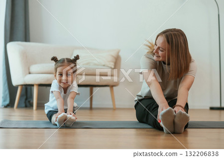 Young woman with little girl are doing yoga at home Young woman with little girl are doing yoga at home 132206838