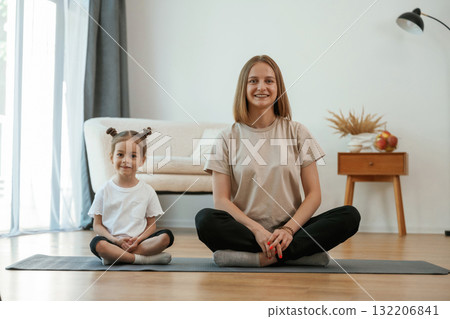 Smiling, positive facial expression. Young woman with little girl are doing yoga at home 132206841