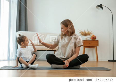 Smiling, positive facial expression. Young woman with little girl are doing yoga at home Smiling, positive facial expression. Young woman with little girl are doing yoga at home 132206842