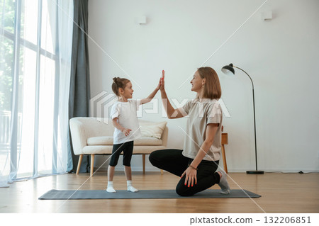 Well done, doing high five. Young woman with little girl are doing yoga at home 132206851