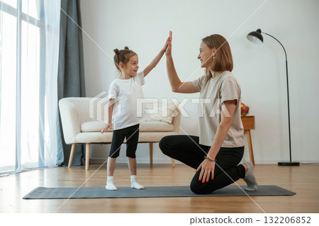 Well done, doing high five. Young woman with little girl are doing yoga at home 132206852