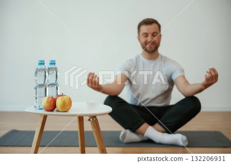 Bottles of water and apples. Yoga man is sitting on a mat at home Bottles of water and apples. Yoga man is sitting on a mat at home 132206931