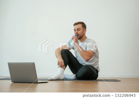Man is sitting on the yoga mat with laptop on the floor Man is sitting on the yoga mat with laptop on the floor 132206943