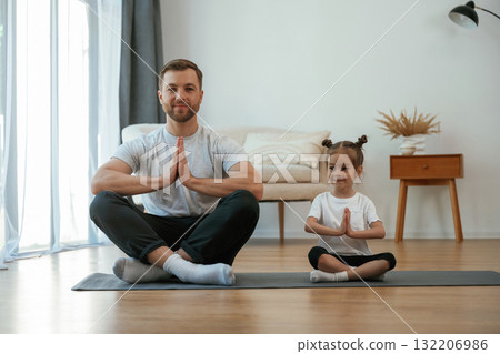Lotus pose. Father with little daughter are doing yoga at home Lotus pose. Father with little daughter are doing yoga at home 132206986